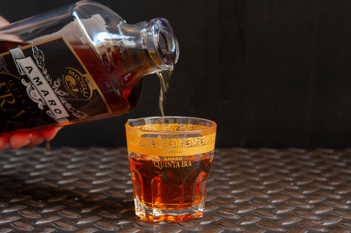 cocktail-3920 Bottiglia di amaro quinta era versato in un bicchiere su sfondo nero